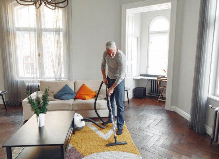 : A man vacuuming a rug in a bright living room, using effective techniques to speed up drying time after carpet cleaning