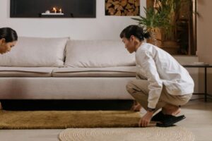 Two people lifting a rug in a cozy living room, ensuring proper airflow for faster carpet drying after cleaning.